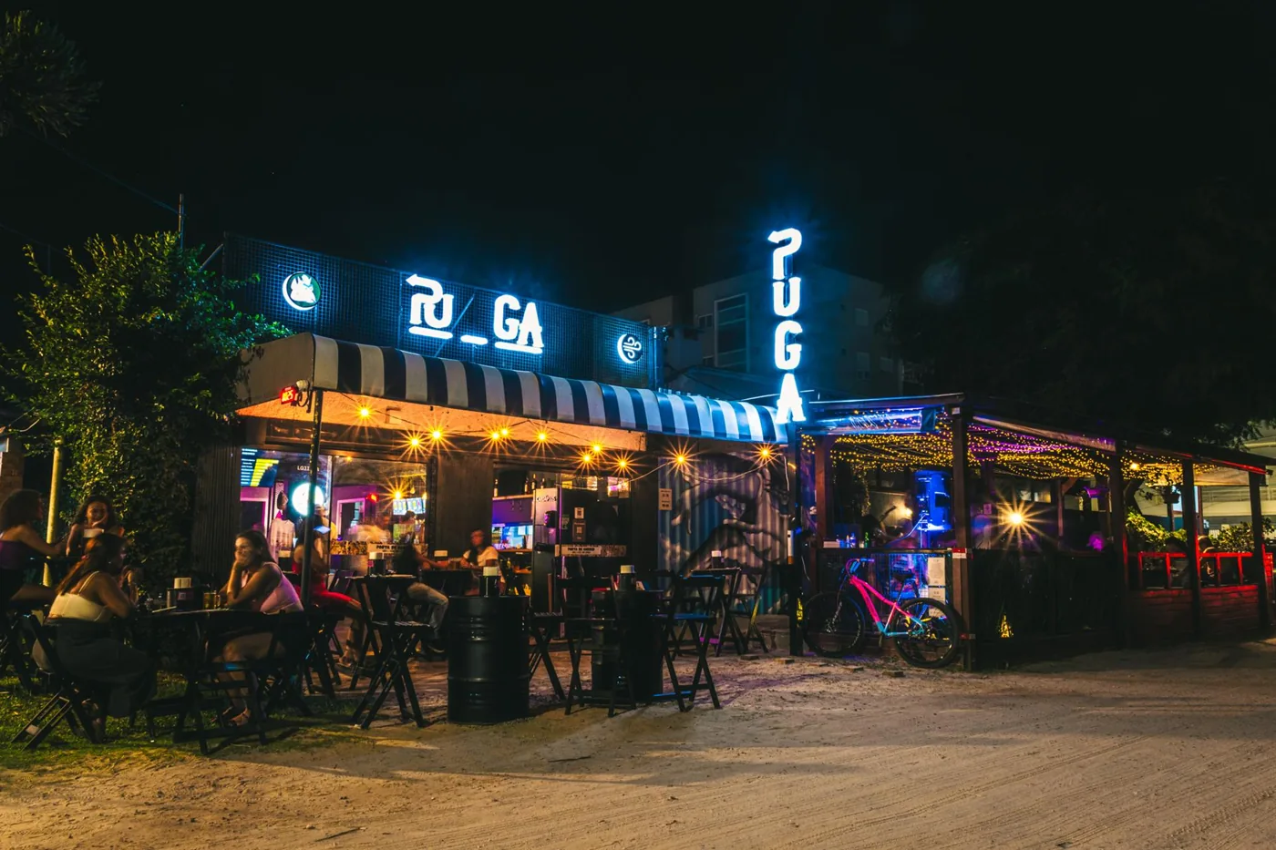 Mesas na rua de areia e fachada iluminada do PUGA Cassino